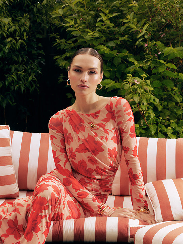 Woman in a red floral dress sitting on a striped sofa with greenery in the background