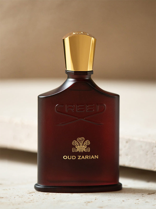 Brown Creed perfume bottle with gold cap on a beige background