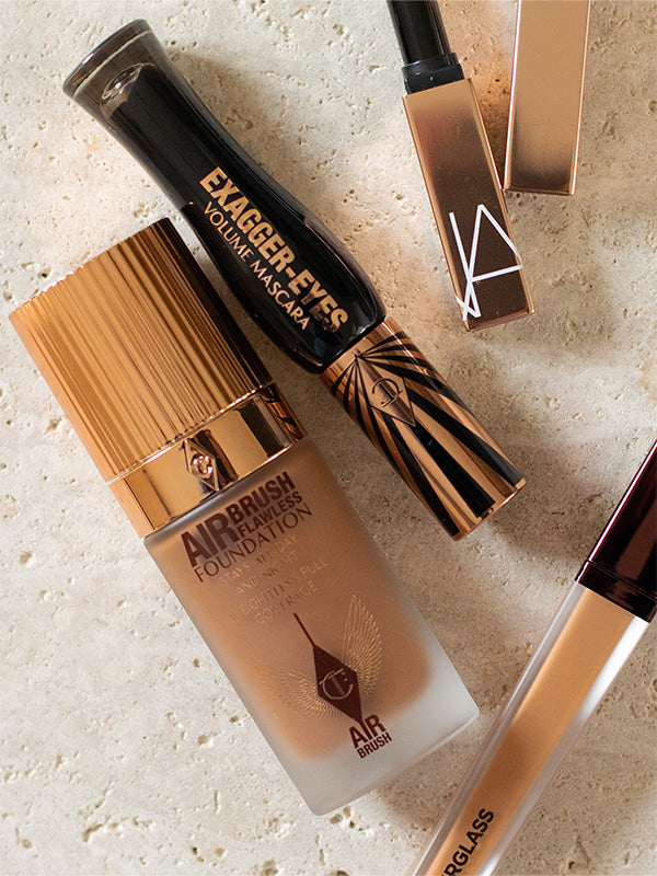 Makeup products including a foundation bottle and two lipsticks on a textured surface