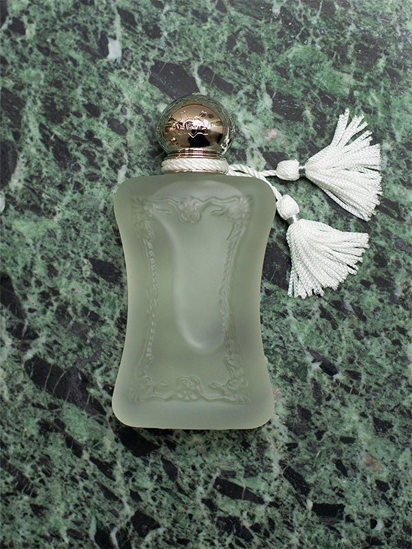 Frosted perfume bottle with gold cap and white tassel on a green marble surface