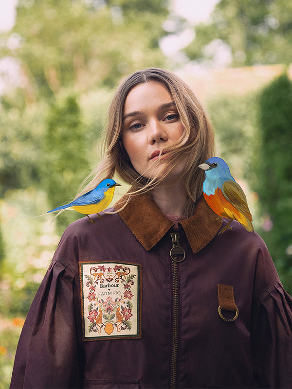 Woman wearing a brown jacket with birds perched on it, outdoors.