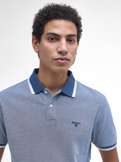 Man wearing a blue and white polo shirt with a Barbour logo on a plain background