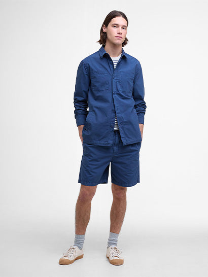 Man with long brown hair wearing a blue shirt and shorts on a white background