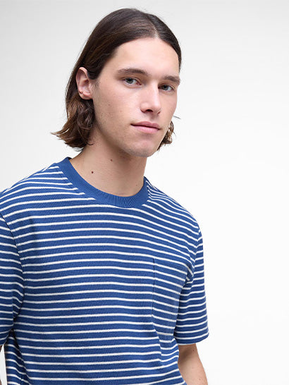 Man with long brown hair wearing a blue and white striped t-shirt against a plain background