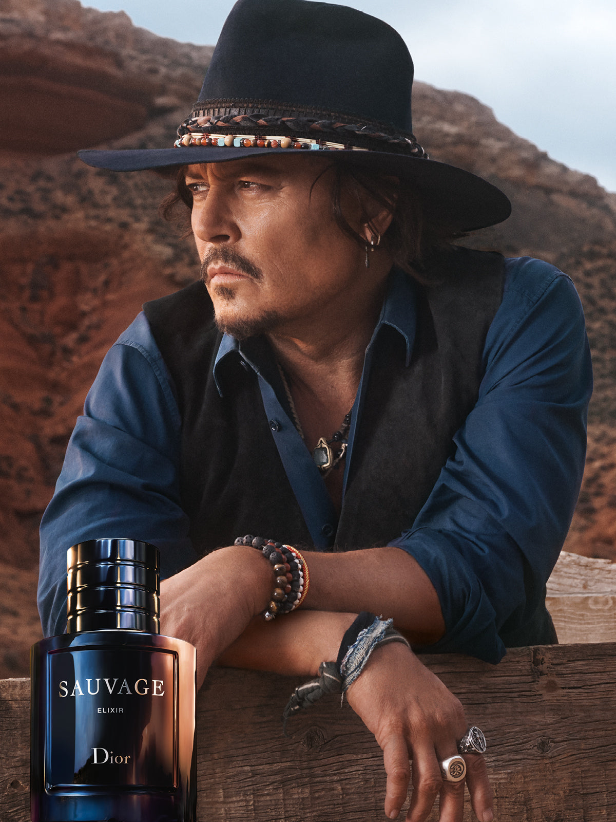 Man in a cowboy hat with a Dior Sauvage perfume bottle in a desert setting